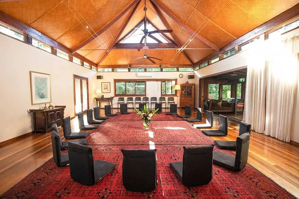 The meditation hall at Sangsurya, with floor seats in a circle on a red rug under a high timber ceiling